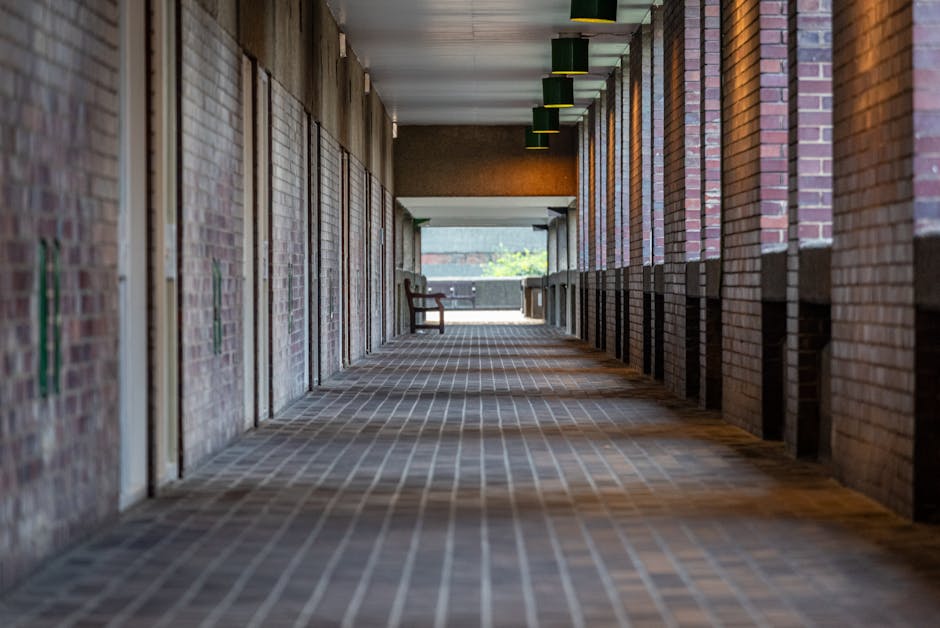 A professional cleaner from Oakleigh Park Carpet Cleaners is performing surface cleaning in a spacious, well-lit communal hallway. The worker, dressed in a dark uniform, is standing beside a cleaning 